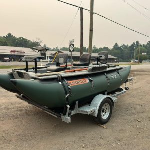 Towable fishing boats with seats in a pickup-area trailer, near a storefront and power poles in a gravel lot.
