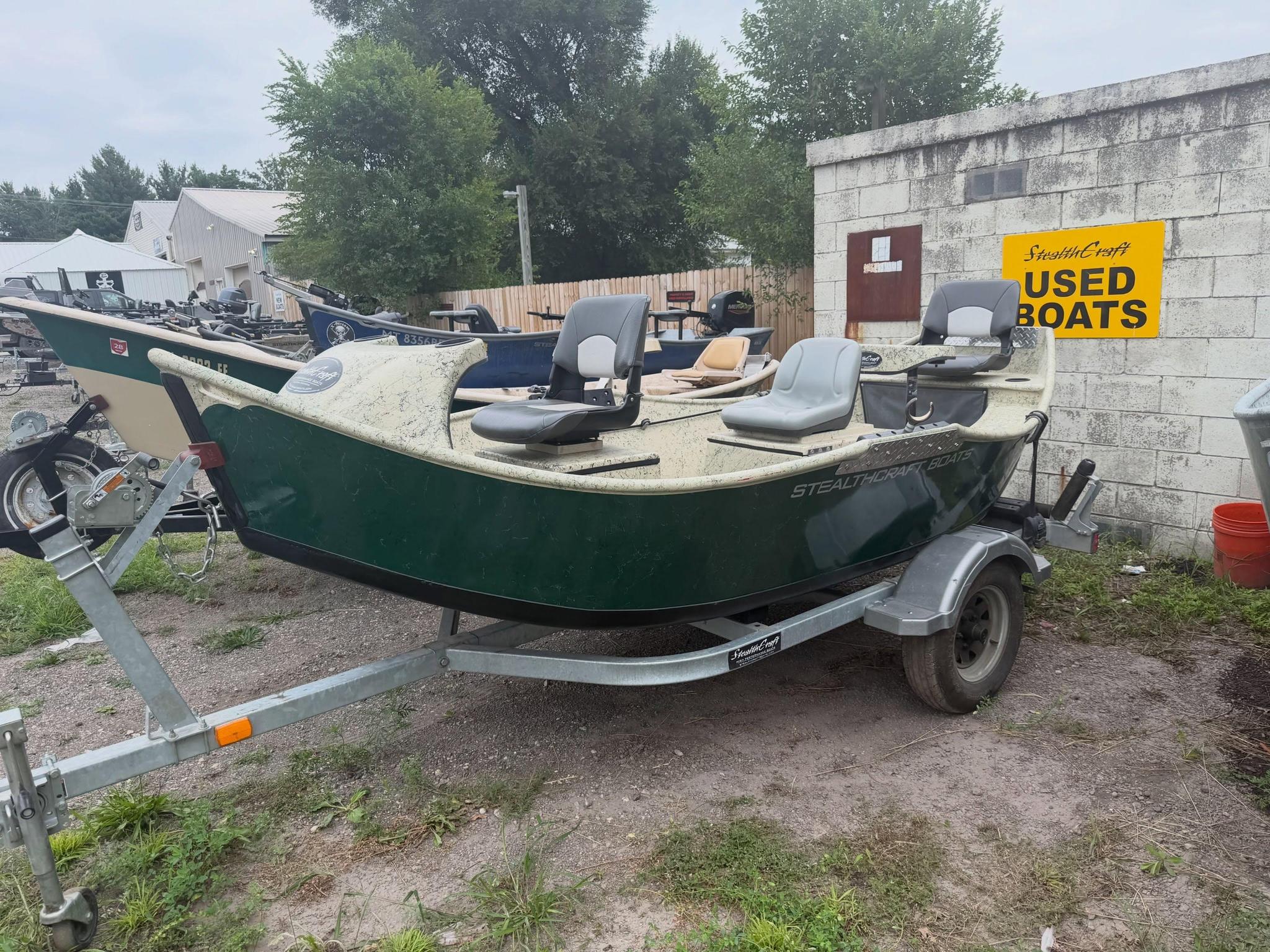 Boats on a trailer in a boatyard with a yellow 'USED BOATS' sign on a concrete wall behind them.